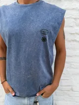Musculosa sin mangas, color azul desgastado (acid wash), con estampado gráfico en la espalda que incluye el texto "OSTEN THE WORLD IS YOURS KEEP MOVING KEEP DREAMING" y un diseño de elipses entrelazadas.