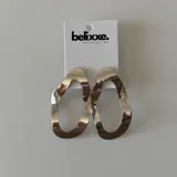 Par de aros colgantes con forma ovalada irregular, disponibles en plateado y dorado.