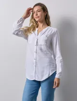 Camisa blanca de lino y rayón, con cuello a la base y escote en V abotonado. Tiene dos bolsillos con botón en el pecho y mangas largas regulables con presilla y botón.