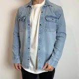 Chaqueta de jean celeste con corte regular, cuello camisero, cierre con botones a presión, dos bolsillos con solapa abotonada en el pecho y mangas largas con puños abotonados.