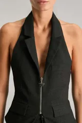 Chaleco negro con cuello halter y solapas sastreras. Cuenta con cierre frontal con cremallera metálica, espalda cavada y lazo de ajuste con avío metálico. Confeccionado en bengalina con efecto metalizado.