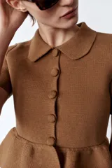 Chaqueta color marrón de tejido de punto, con cuello solapa, manga corta y bajo evasé con volantes. Cierre frontal con botones forrados a tono.