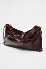 Bolso de hombro marrón oscuro con acabado brillante, asa trenzada y ojales metálicos en los laterales.