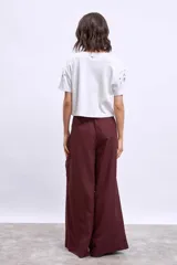 Remera blanca de algodón con cuello redondo y mangas cortas. Presenta apliques metálicos y aberturas circulares en los hombros y el frente.