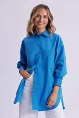 Camisa celeste de manga larga, corte oversize, con cuello clásico, cierre frontal con botones, bolsillo en el pecho y bajo redondeado.