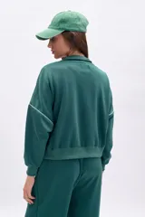 Campera deportiva de tejido de punto color verde oscuro, con cierre frontal plateado y cuello alto. Presenta vivos blancos que delinean el canesú y los puños y cintura son de elástico.