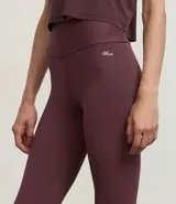 Legging deportiva ajustada al cuerpo, color morado oscuro, con cintura alta y bolsillo pequeño en la espalda.