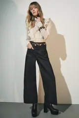 Pantalón de jean de tiro alto color negro con pierna ancha, bolsillos delanteros y traseros, y cierre frontal con cremallera y botón metálico.