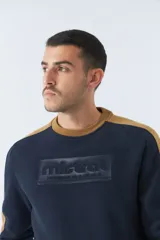 Buzo de felpa azul marino con cuello redondo y puños. Tiene mangas largas y calce regular. Presenta un logo estampado en relieve en el pecho y un logo de goma en la manga.