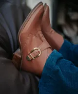 Bota corta color marrón con textura tipo piel de reptil, hebilla dorada y taco medio de madera.