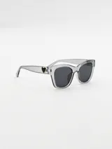 Lentes de sol de acetato color gris transparente, con forma cuadrada y detalle de corazón dorado en el lateral.