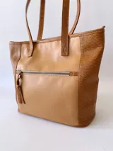 Bolso tipo tote de cuero color camel con paneles laterales texturizados. Tiene doble asa de hombro, cierre superior con cremallera y bolsillos internos.