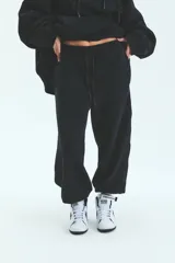 Pantalón de jogging negro de frisa esmerilada con cintura y botamanga elastizada, cordones de algodón con puntera termocontraíble y bolsillos laterales.