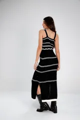 Vestido largo de punto calado blanco con rayas horizontales negras y breteles finos. El vestido tiene un corte recto y aberturas laterales en el ruedo. Las modelos llevan sombrero de estilo cowboy y botas de cuero.