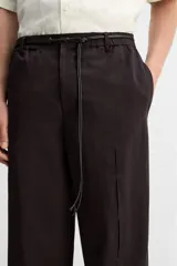 Pantalón relaxed fit color marrón oscuro confeccionado en tejido con mezcla de algodón y lino. Cintura elástica, bolsillos laterales y bolsillo trasero de plastrón. Perneras con pliegues frontales. Cierre en delantero con cremallera y botón.