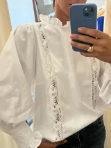 Camisa blanca de mangas largas abullonadas con detalles de encaje y cuello con volados.