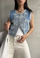 Chaleco de jean celeste con bordado floral blanco, corte recto y cierre frontal con botones.