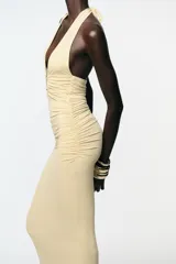 Vestido midi color crema de poliamida con cuello halter con lazada, escote pico pronunciado, detalle de pieza metálica y tejido con frunces.
