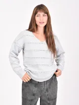 Buzo de tejido de punto gris claro, con cuello en V y detalles calados horizontales a lo largo del cuerpo y mangas. Tiene puños y ruedo acanalados.