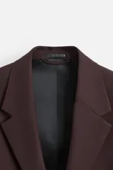 Blazer color borgoña de corte regular, con cuello de solapas de muesca, manga larga con puños abotonados, bolsillos de doble vivo en la cadera, bolsillo interior, abertura en el centro de la espalda y cierre frontal con botonadura.