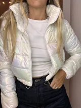 Campera puffer corta, acolchada, con acabado iridiscente que refleja tonos pastel. Posee cuello alto y cierre frontal con cremallera.