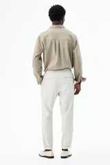 Pantalón de vestir gris claro, de corte slim fit, con cintura elástica y cordón ajustable. Presenta bolsillos laterales y traseros ribeteados, pliegues cosidos y doblez en el bajo.