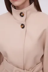 Chaqueta color beige con cuello alto, mangas anchas y cinturón.