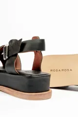 Sandalias negras de cuero con plataforma y tiras cruzadas en el empeine y tira con hebilla alrededor del tobillo.