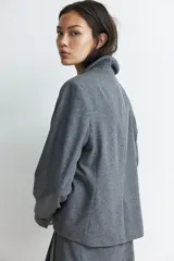 Blazer gris de corte entallado, con solapas de muesca, botonadura sencilla, bolsillo superior insertado y bolsillos delanteros. Tiene hombreras, botón decorativo en los puños y abertura atrás.