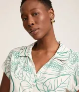 Camisa blanca con estampado floral en tonos verdes, de manga corta, cuello camisero y escote en pico. Tiene cierre con botones y lazo en el bajo.