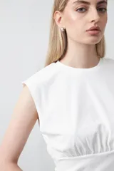 Top sin mangas color beige, confeccionado en tejido acanalado. Presenta hombreras definidas y un recorte fruncido bajo el busto que ajusta la silueta.