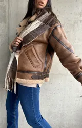 Campera marrón de cuero sintético con interior de piel sintética color beige. Tiene cierre frontal con cremallera, cuello con hebilla y bolsillos laterales.