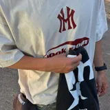 Camiseta oversize color crema con efecto acid wash, de alto gramaje (240 grs). Estampado trasero en serigrafía unicolor bordó con la inscripción "LOOKMOM SPORTS" y un logo con la letra "L".