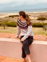 Sweater gris con diseño geométrico en negro y rojo alrededor del cuello, de lana tejido a mano con estilo nórdico.