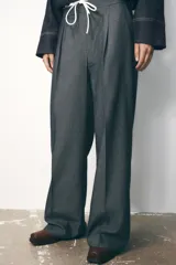 Pantalón ancho gris con textura de espiga, tiro alto, doble cintura elástica ajustable con cordón, pinzas frontales, bolsillos delanteros y falso bolsillo de vivo en la espalda.