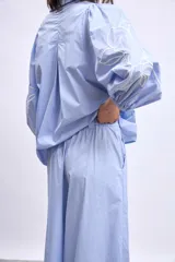 Pantalón ancho de algodón color celeste claro, con bordados de flores blancas en los bajos. Presenta un corte de tiro alto con pliegues frontales y cierre de botón visible.