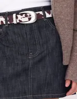 Cinturón de cuero sintético con estampado de vaca y hebilla metálica plateada.