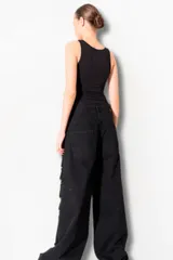 Pantalón de jean negro con corte amplio y múltiples roturas grandes a lo largo de ambas piernas.