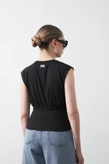 Top sin mangas color beige, confeccionado en tejido acanalado. Presenta hombreras definidas y un recorte fruncido bajo el busto que ajusta la silueta.