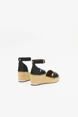 Sandalia de cuero vacuno color negro con taco tipo cuña revestido en yute. Presenta una tira ancha sobre el empeine y una pulsera ajustable al tobillo con cierre de hebilla metálica.