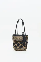 Bolso tote tejido en raffia color negro y beige, con vivos y correas en cuero sintético negro. Tiene cierre interno con snap metálico y forro de algodón.