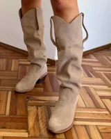 Bota alta de cuero color beige, estilo texana, con caña alta y taco bajo.