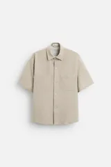 Sobrecamisa color beige de tejido elástico, con cuello solapa, manga corta y bolsillos de parche en el pecho. Cierre frontal con botones a presión.