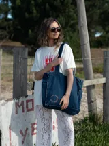 Bolso tote de denim azul oscuro con asas de hombro y detalle de bordado circular con texto en el frente.