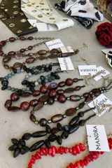 Conjunto de collares de cuentas de diferentes colores y materiales, incluyendo cuentas de piedra, madera y cristal. Los collares tienen cadenas doradas y etiquetas blancas con la marca "MANDRA".