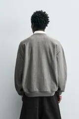 Sudadera gris con rayas verticales blancas, cuello redondo, manga larga y bordado con texto en el pecho.