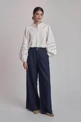 Camisa blanca de mangas largas abullonadas con detalles de calado en los puños, cuello mao y cierre frontal con botones.