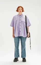 Camisa de manga corta color lavanda con doble bolsillo y ojal delantero con solapa en uno de ellos. Tiene calce oversize y está realizada en tejido plano suave al tacto.