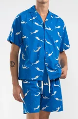 Camisa azul con estampado de sirenas blancas, de corte recto, manga corta y cuello camisero.