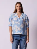 Blusa de gasa estampada con flores blancas sobre fondo celeste, marca Floral & Ivy. Cuello a la base con escote en V. Manga corta con detalle de puño y botón.